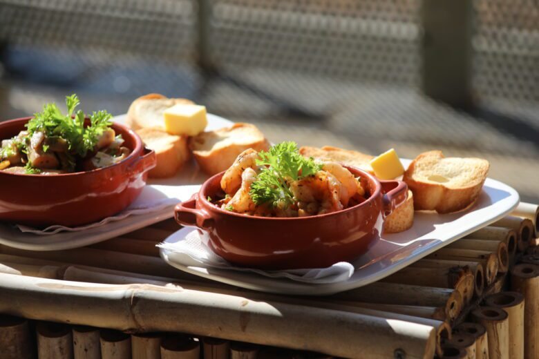 Two red ceramic bowls filled with a shrimp dish, garnished with parsley, served with slices of toasted bread and butter on a white tray.