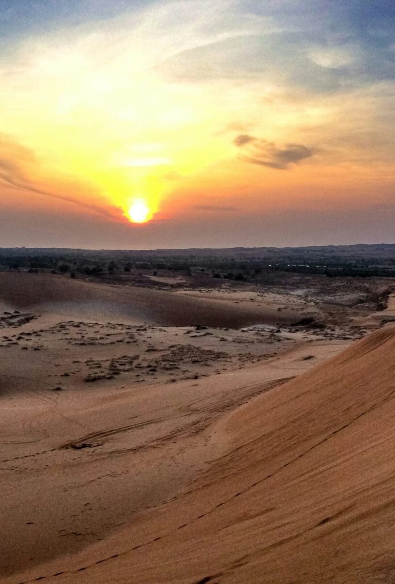Golden sunset over sweeping desert sand hill with a wide sky painted in soft orange and blue hues in Mui Ne.