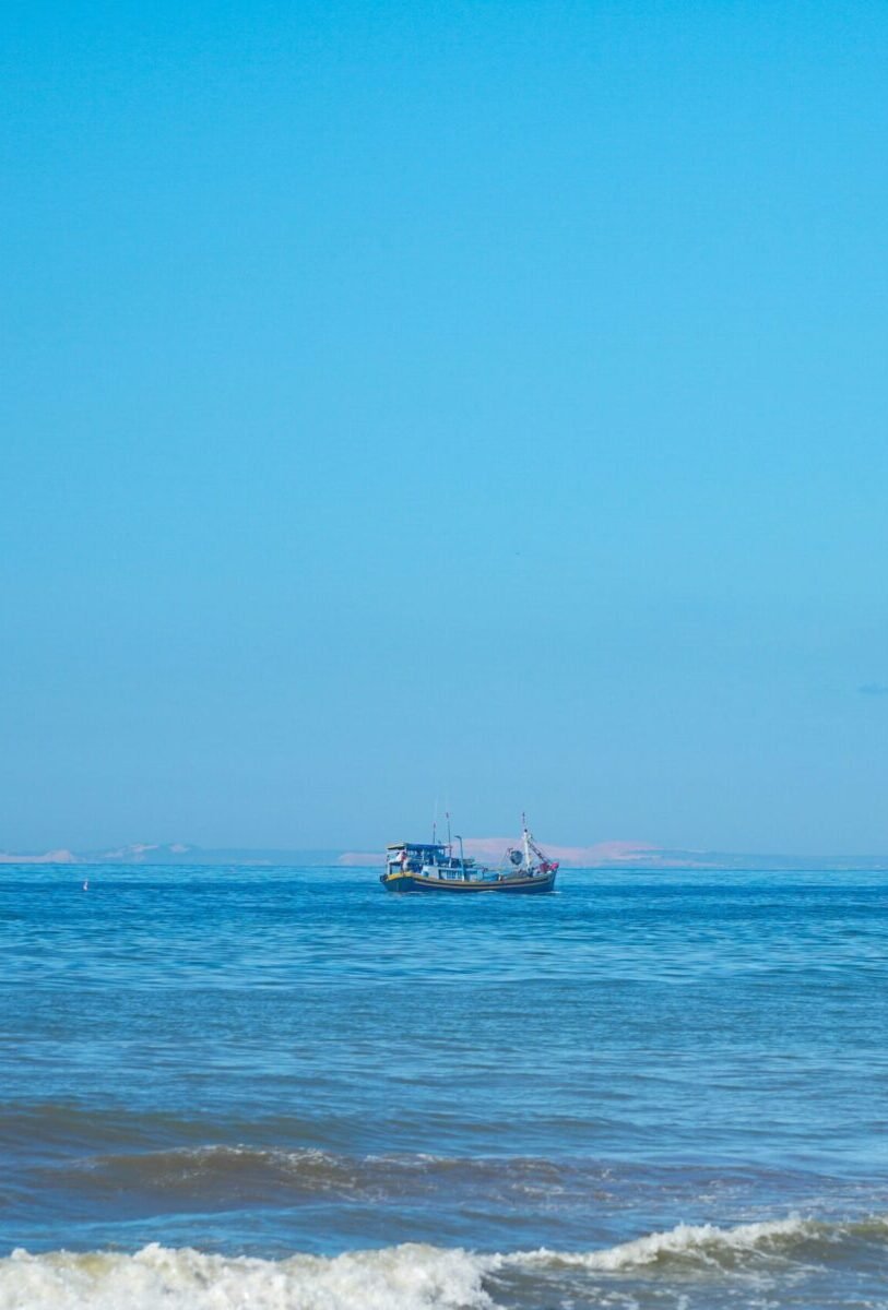 A fishing boat floats peacefully on a calm blue sea under a wide open sky in Mui Ne.