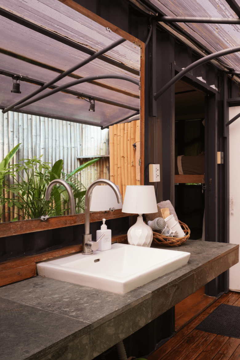 Modern outdoor vanity sink with mirror, lamp, and basket of towels at Cargo Remote.