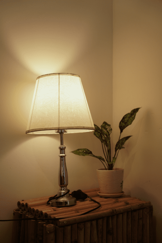 Cozy corner with a lit table lamp and a potted plant on a bamboo nightstand.